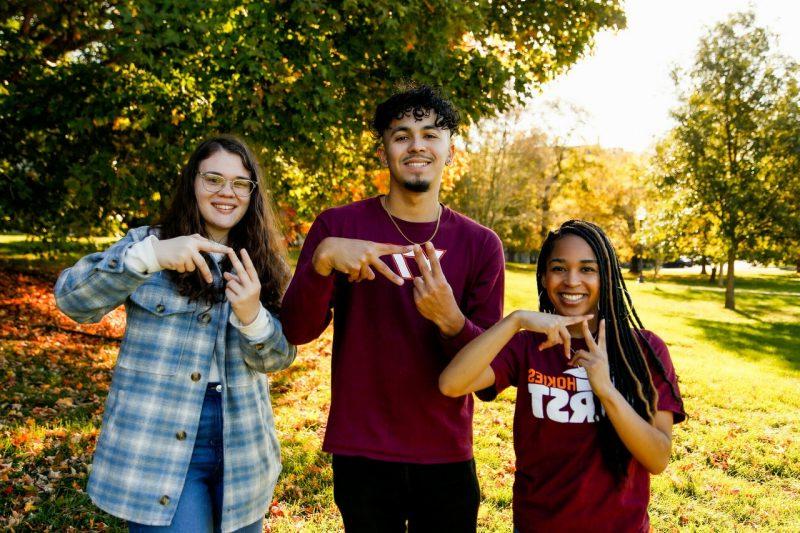 三位第一代学生在布莱克斯堡校园里展示着“VT”的手势，享受着秋天的一天.